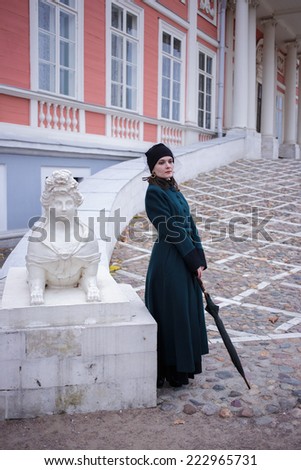 Full-length portrait of a pretty woman in vintage autumn clothes standing in front of old city buildings