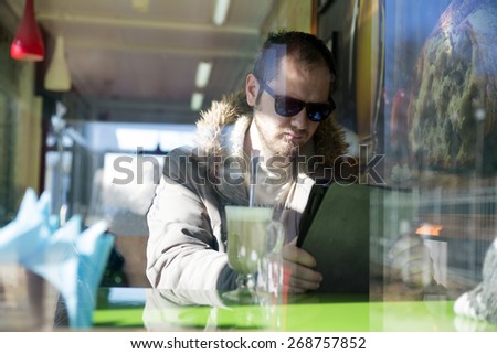 Russian man with beard sitting inside a cafe in glasses. Photo over the window