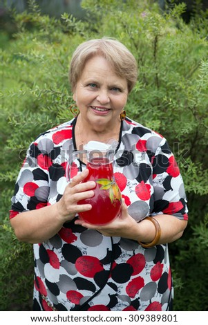 Smiling senior woman showing jug with fresh stewed fruit