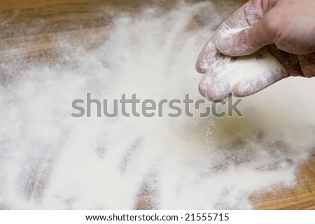 a hand is throwing flour to kitchen desk