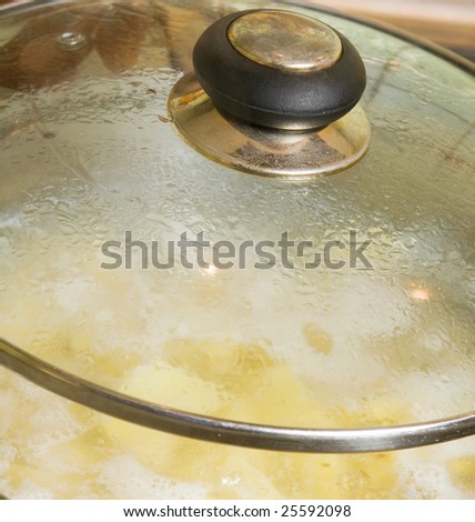 Boiling potatoes in hot water in a pot with glass lid