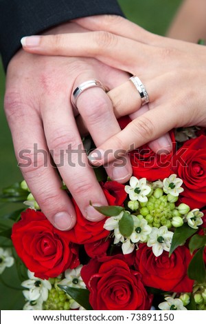 Wedding details - closeup of hands of newly-married with gold rings on wedding bouquet