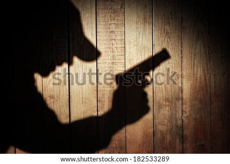 Man in silhouette with gun ready to shoot on natural wooden background, with space for text or image.