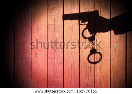Male Hand shadow with Gun and Handcuffs on Natural Wood Background, with space for text or image.