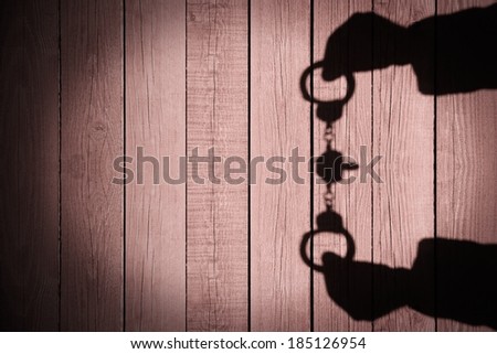Human Hands Shadow with Handcuffs on Natural Wooden Background. You can see more silhouettes and shadows on my page.