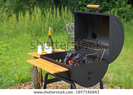 Classic Barrel Grill Appliance On The Backyard Lawn. Outdoor BBQ Grill Appliance. Barbeque Charcoal Barrel Flaming Hot Grill Ready For Cooking Cookout Food On Backyard Lawn. Garden Party Concept.