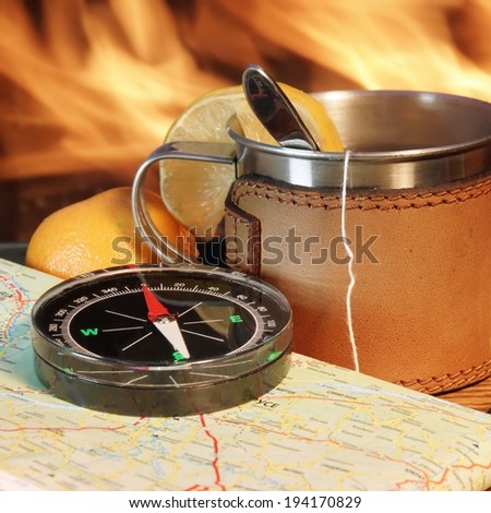 Compass, Map, Mug, Teabag and lemon on wood board. Flames in background.