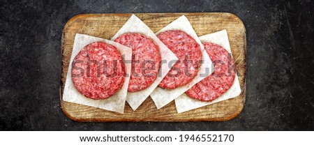 Homemade Beef Burgers on Wooden Board, Top View. Four Raw Ground Beef Meat Steak Burgers Cutlets on Black Table Background, Overhead View. Farmers Uncooked Beef Burgers for BBQ Grilling Or Frying.
