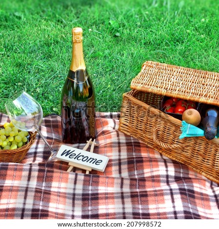 Picnic setting with Champagne wine, glasses, grape and picnic hamper basket. Small board with sign 