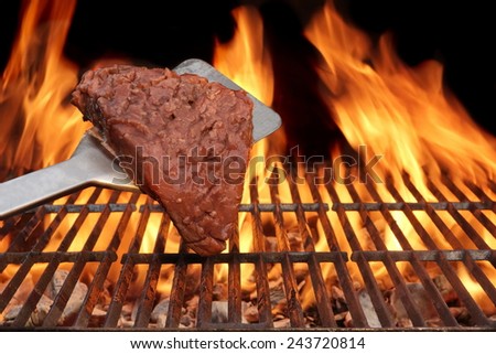 Flame Broiled Steak and Spatula on the BBQ Grill. Flames on the black Background.