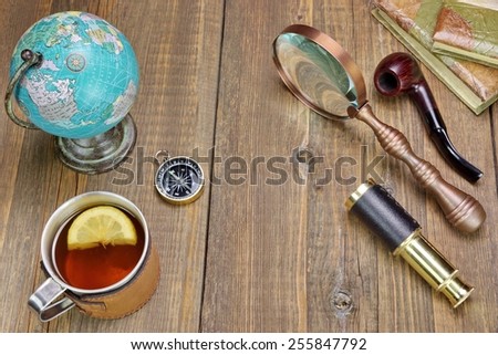 Tea Mag On Grunge Wood Table With Many Travel Objects. Compass, Spyglass, Vintage Notebooks, Bell, Retro Globe Map, Smoking Pipe, Magnifying Glass