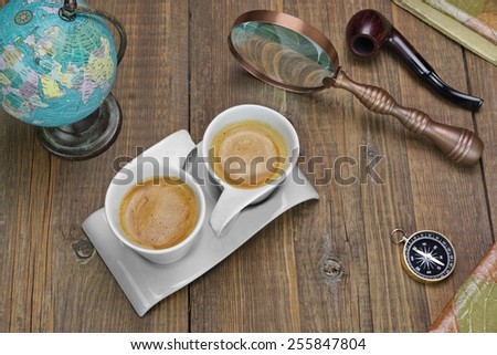 Two Coffee Cups And Adventure Objects On The Wooden Table. Compass, Old Globe Map, Vintage Notebooks, Smoking Pipe, Vintage Magnifying Glass