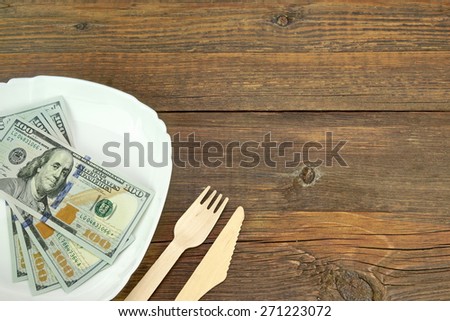 White Ceramic Plate With USA New One Hundred Dollar Bills, Wooden Fork And Knife On Rough Wood Background Or Texture With Copy Space