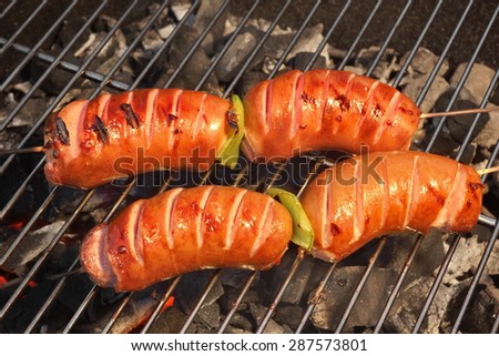 Four Tasty Sausages On The Hot Barbecue Charcoal Grill Close-up. Good Snack For Summer Outdoor BBQ Party Or Picnic