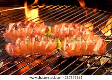 Fatty Sausages On The Hot Barbecue Charcoal Grill And Flames In The Background Closeup