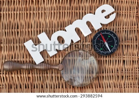 White Wood Sign Home, Retro Magnifying Glass And Modern Magnetic Travel Compass On The Rustic Wicker Background