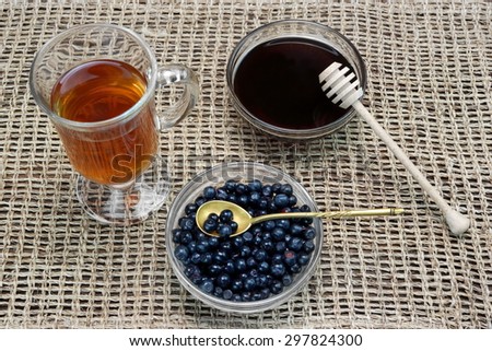 Full Tea Cup With Herbal  Tea, Glass Plate With  Bilberry, Lime Tree Dark Honey Gold Spoon On The Wicker Cloth. High Angle View