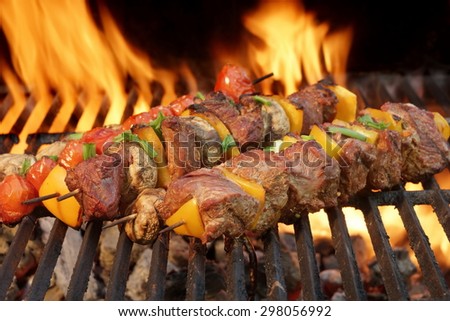 Close-up Of BBQ Tasty Cubed Beef Kebabs With Paprika Slice On The Flaming Charcoal Grill In The Background
