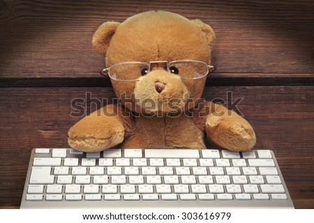 Cute Teddy Bear With A Wireless Keyboard In Front Of An Imaginary Computer Screen At Wooden Wall In Lanters Light. Internet Surfing Or Computer Work Concept