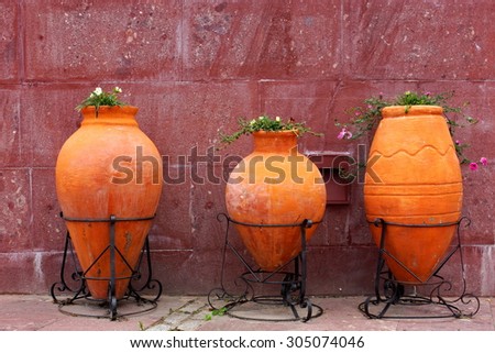 Street Decoration. Three Large Clay Jars With Flowers On The City Street At The Tilled Red Wall