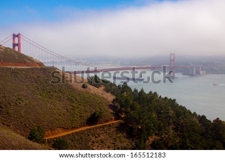 The Golden Gate bridge seen from the Golden Gate National Recreation Area. The fog is getting to move out while a vessel is crossing under the bridge to move into the bay.