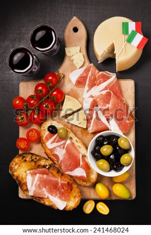 prosciutto,  cheese parmesan, olives, cherry tomatoes, red wine on wooden board. rustic snack