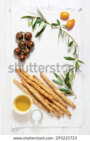 Italian food. space for writing text. colored tomatoes, bread sticks with sesame seeds, olive oil and olive leaf.
