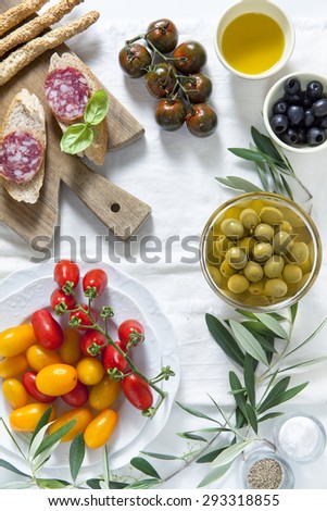 ingredients for a summer snack. summer products. sandwich with salami, red and yellow cherry tomatoes, green and black olives, black Sicilian tomatoes, bread sticks and olive oil.