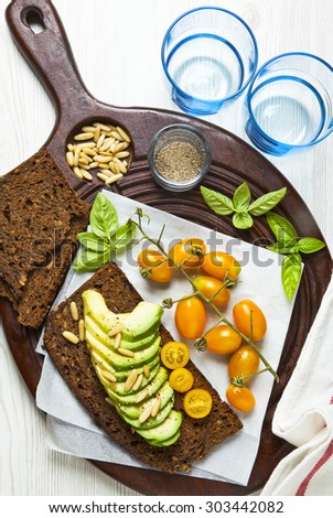 yellow grape tomatoes and avocado with pine nuts. basil leaves. sandwich on white. healthy breakfast.