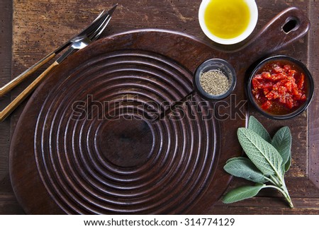 empty board for cutting on the old wooden background and olive oil, sage leaves, milled pepper, fork and knife. tomato sauce. space for writing text advertising.