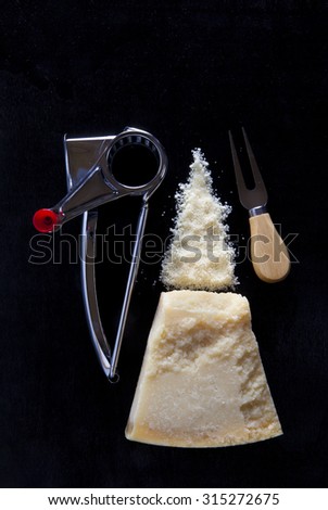 a piece of Parmesan cheese on dark with a manual cheese grater and a knife for chopping hard cheese