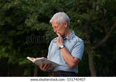 Emotive old man with book in the hands. Blue jeans. Grey t-shirt.