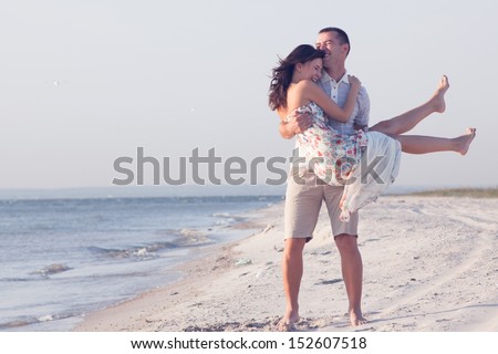 Very happy couple enjoy each other during sunset on the beach. Man holding woman on hands