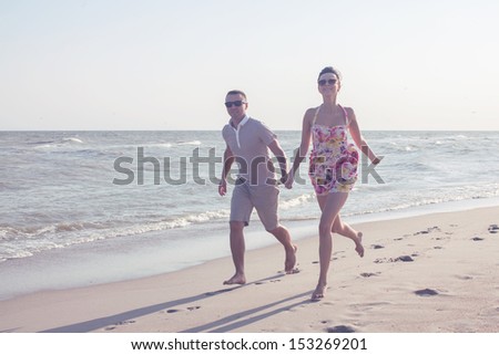 Young happy couple running together among a seashore at sunny day. Casual clothes