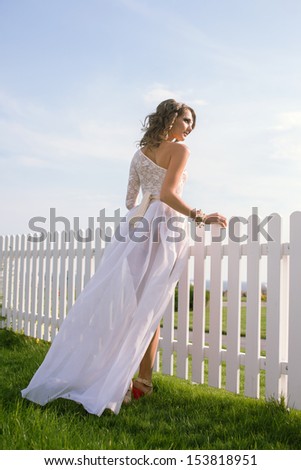 young woman in long white dress standing near white fence