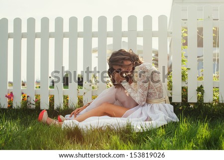 fabulous fashionable woman in long white dress sitting on backyard outdoors. Exclusive beige and white dress. high heels