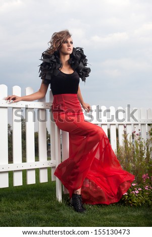 Fashionable model posing in long red and black dress outdoors. Red skirt.  black body. volume accessory on his shoulders. black shoes with spikes