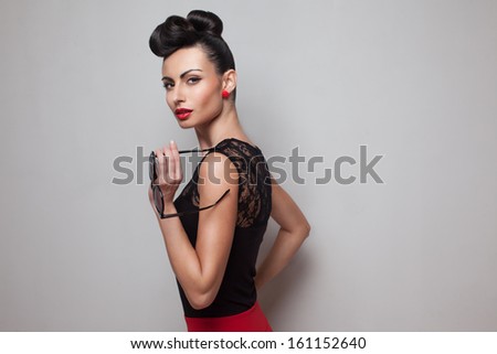 Pin Up style woman holding round sunglasses posing in red skirt. Red lips. Updo, twisted high bun. top knot