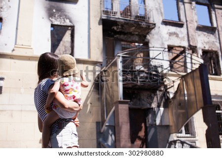 MARIUPOL, UKRAINE - JULY 19, 2015: Mother with baby walking near of destroyed building of Mariupol Police City Department