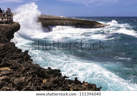 Group of people watching the big waves spraying cascades of water over volcanic cliffs. Costa Tabla, Northern shore of Curacao