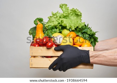 Male hands in black protective gloves hold a box with groceries. Online food delivery concept during quarantine. Fresh vegetables, fruits, food in a wooden box. Delivery from supermarket, farmers Foto stock © 