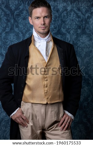 A handsome Regency gentleman wearing a gold waistcoat and black jacket and standing in a room with blue wallpaper and a wooden floor Сток-фото © 