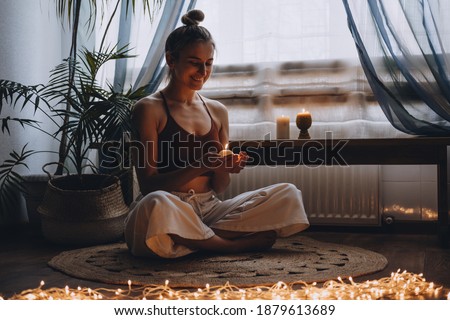 Young woman sitting on the floor, lights candles, enjoy meditation, do yoga exercise at home. Mental health, self care, No stress, healthy habit, mindfulness lifestyle, anxiety relief concept