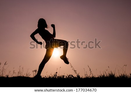 Silhouette of kick boxing girl exercising kick in the nature on sunset sky.