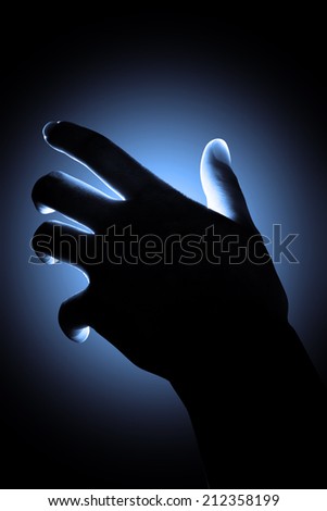 Abstract silhouette hand reaching with blue light background.