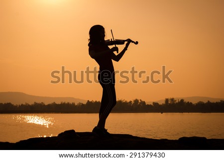 Woman silhouette playing violin in sunrise sky background.