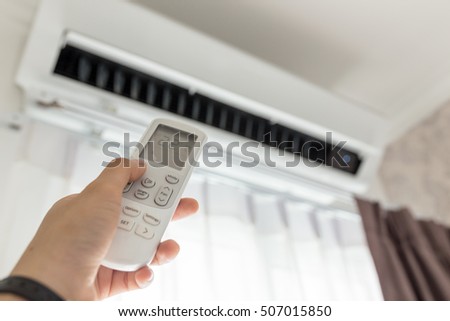 Air conditioner inside the room with woman operating remote controller. / Air conditioner with remote controller 商業照片 © 