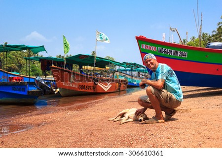 CANDOLIM, GOA, INDIA - 11 APR 2015: Sinquerim-Candolim Boat Owners Association in Goa, India. An unidentified man strokes a dog on the pier.