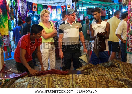 GOA, INDIA - NOVEMBER 23: Goa Night Market on NOV 23, 2014, Goa, India. Unknown family chooses a traditional eastern blanket in the night market in Anjuna.