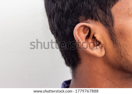 Human Ear - Close up of man ear Its body part helps to hearing sound waves. Face with a human ear and hair. Portrait of indian man and shoes on his ears isolated on white background with copy space.